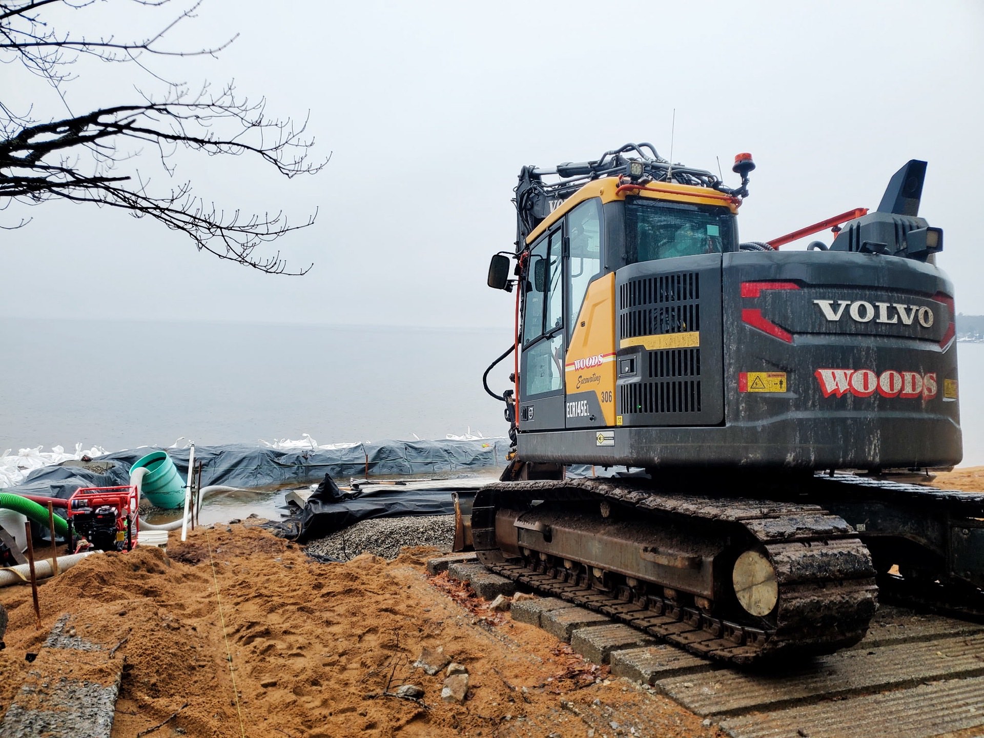 Woods excavator on the Sebago Lake State Park boat ramp site, a sandbag cofferdam and silt barrier holding the lake back and a pump dewatering the work area