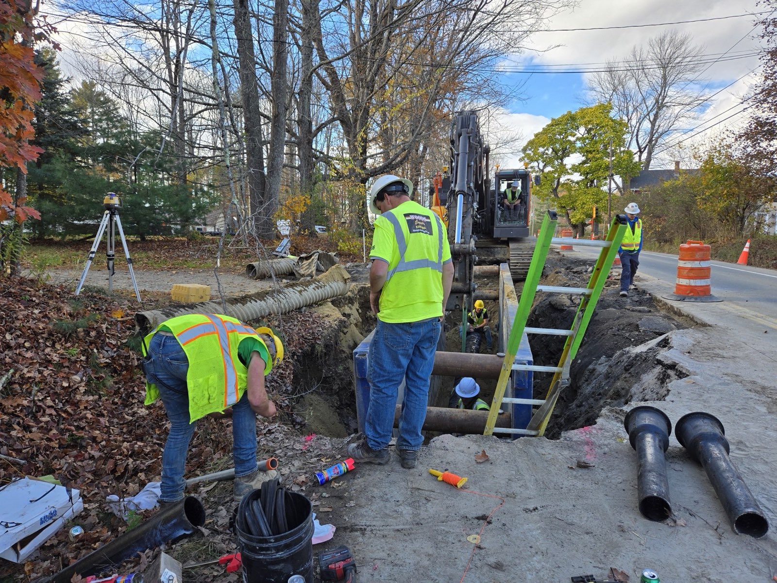 Trench box and ladders set in the Harvard Street water main trench with restrained-joint ductile iron staged and the crew in full PPE