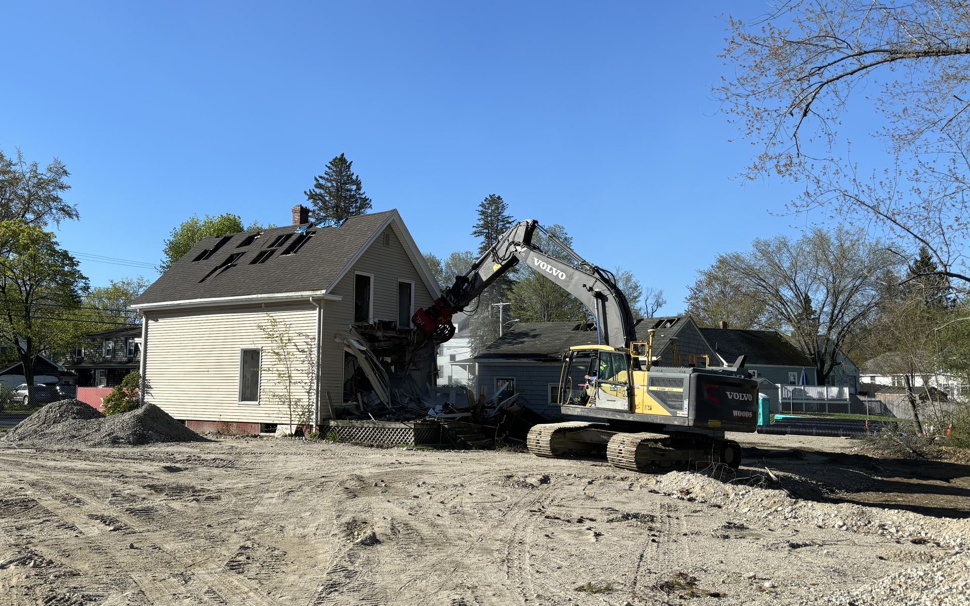 Woods Volvo excavator with a grapple taking down a two-story house, the roof already opened