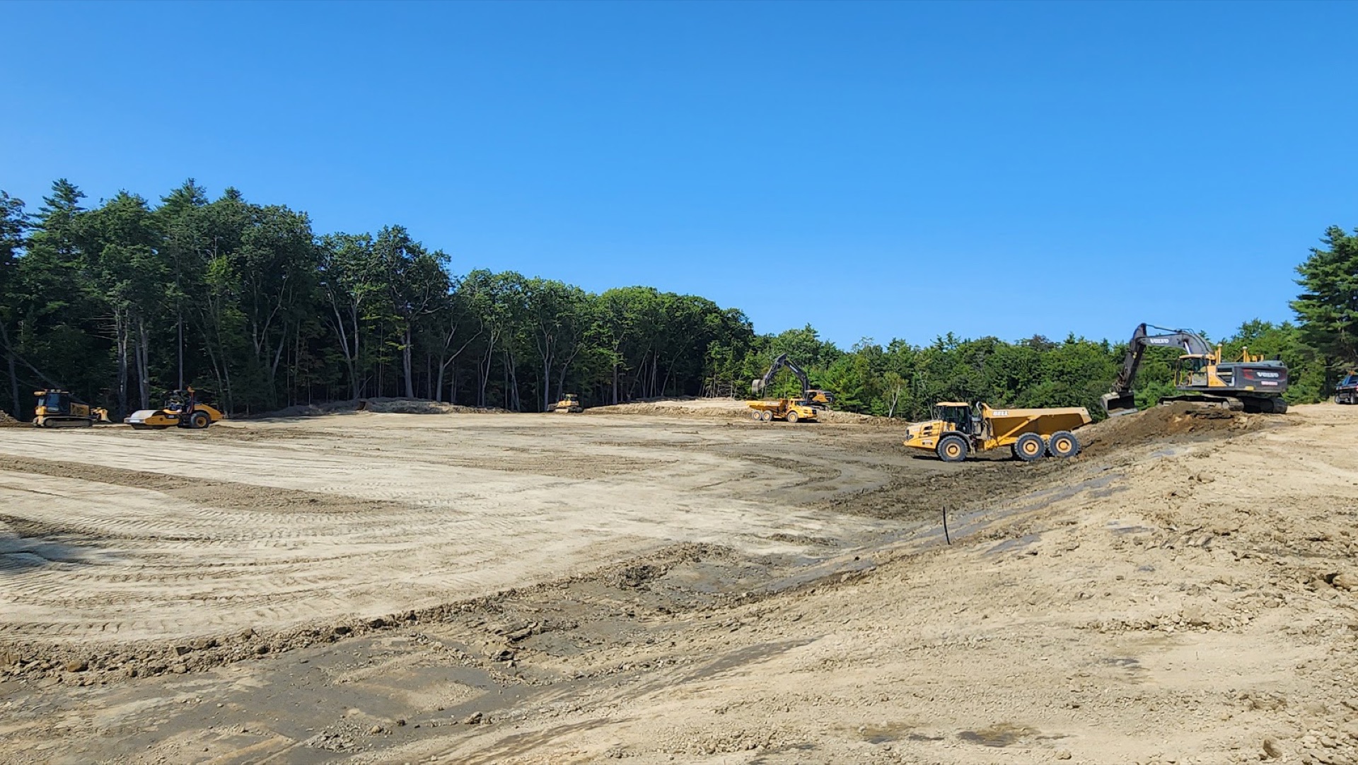 Six Woods machines grading one pad: excavator, two articulated haulers, dozer, and two rollers
