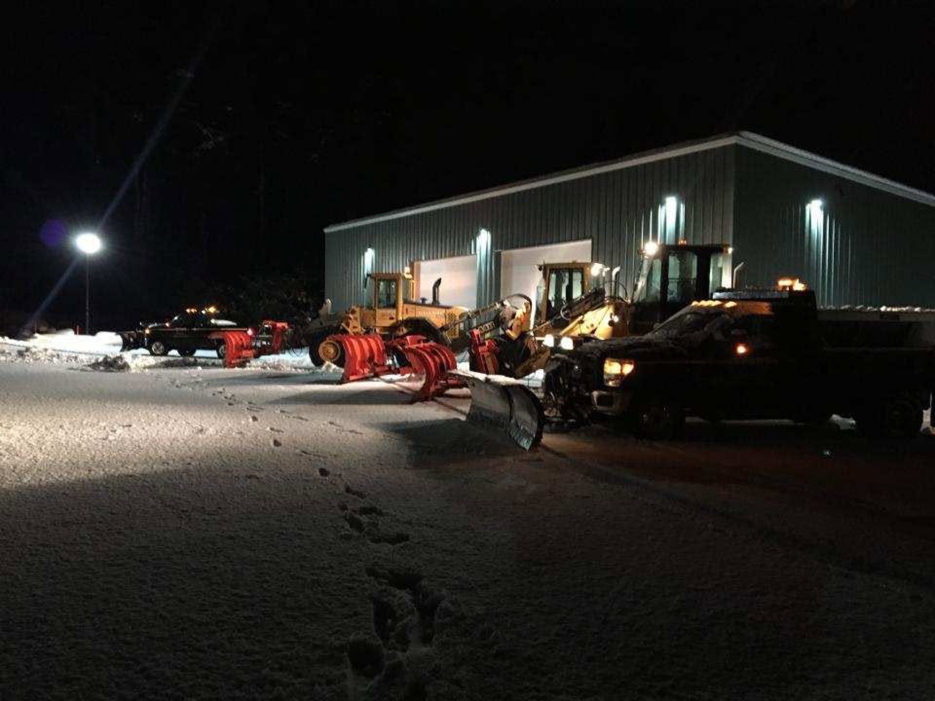 Woods loader with a pusher box and a wing plow truck clearing a lot at night in falling snow