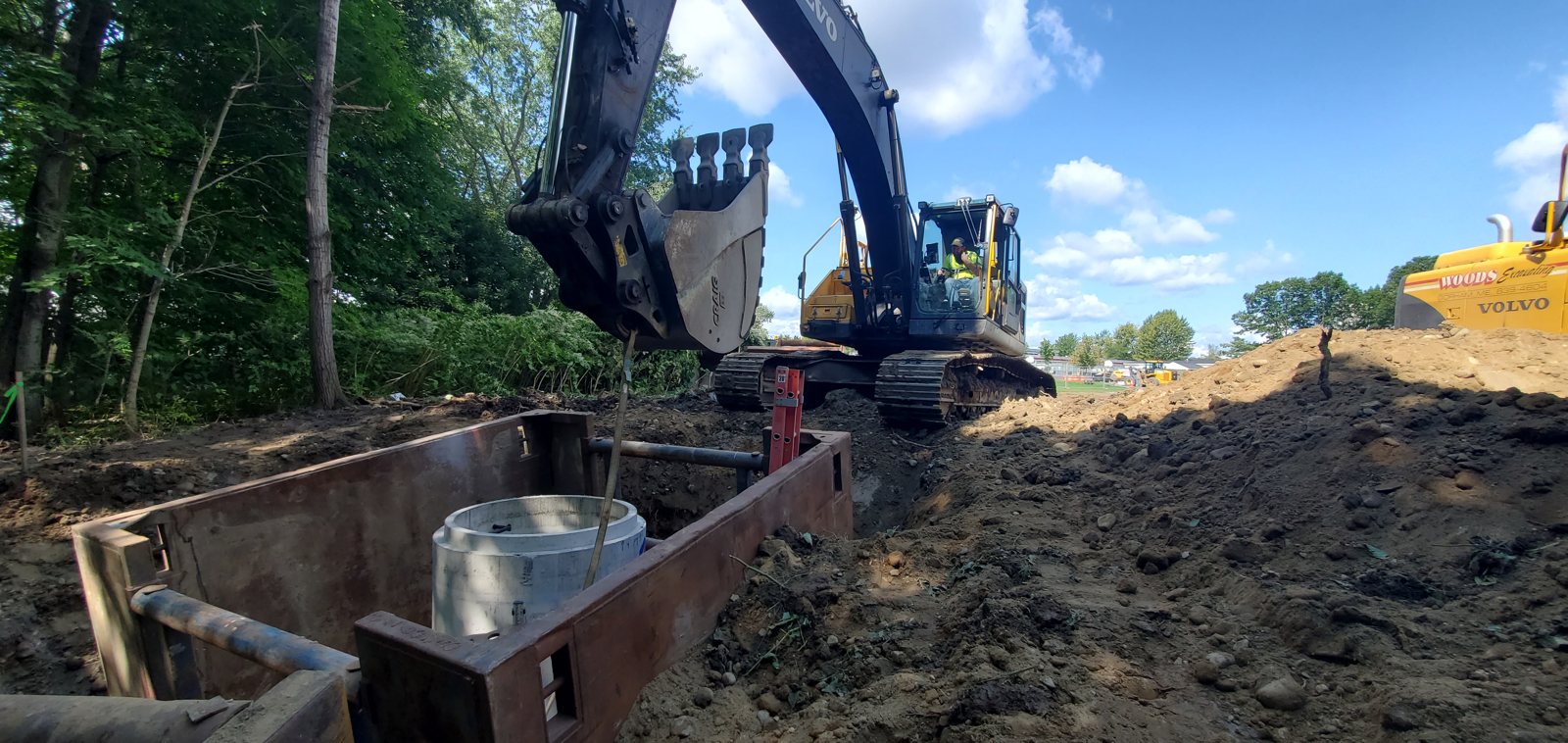 A Woods excavator setting a trench box structure over an open utility trench