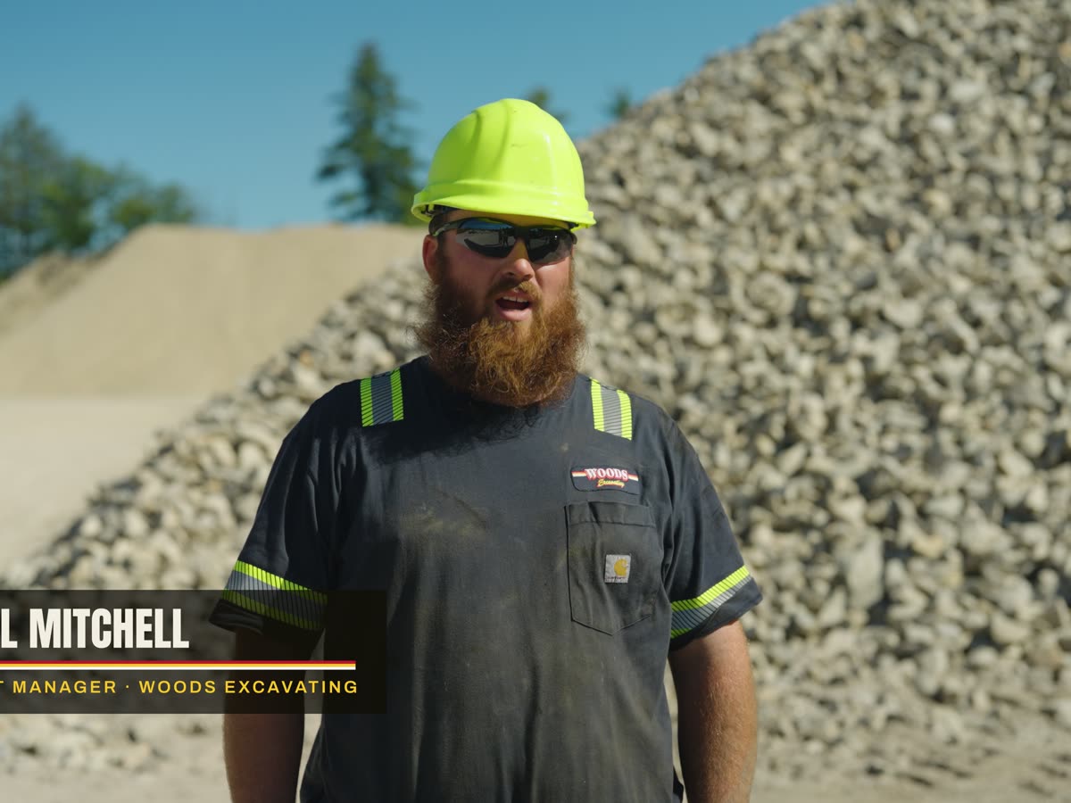 Will Mitchell in a yellow hard hat and hi-vis shirt in front of the crushed stone pile